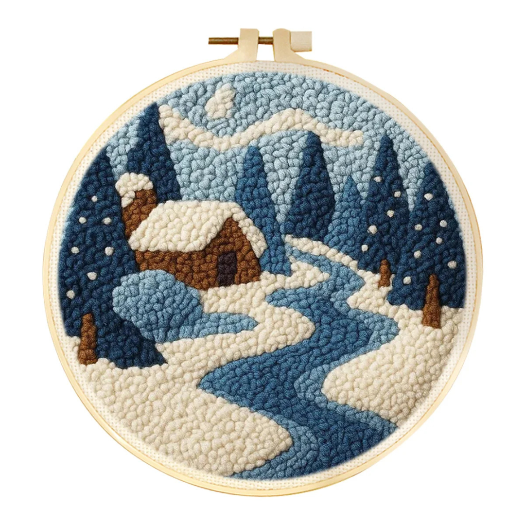 Embroidery hoop with a winter landscape design featuring mountains and a cabin.