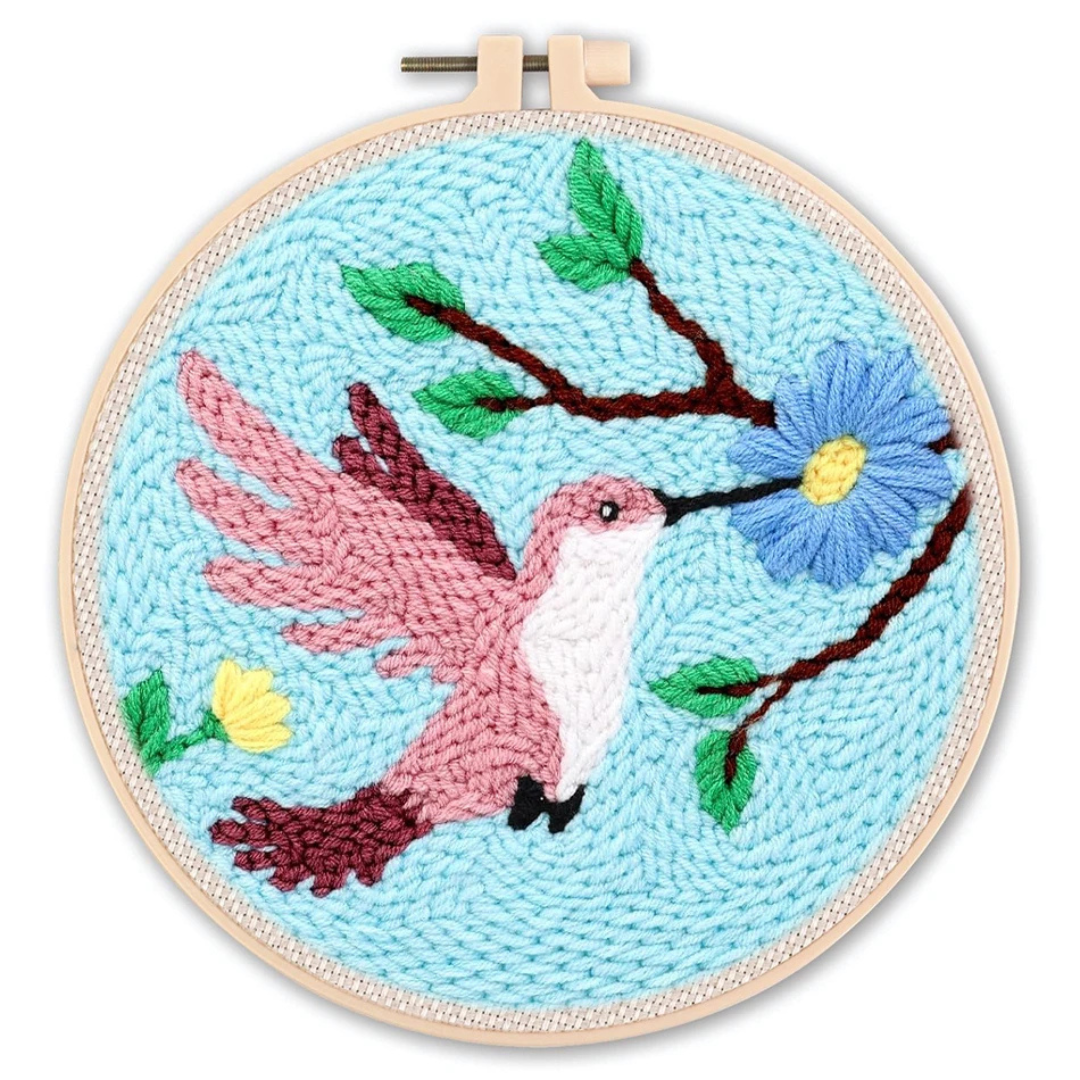 Embroidery hoop with a pink hummingbird and blue flower design on a light blue background.